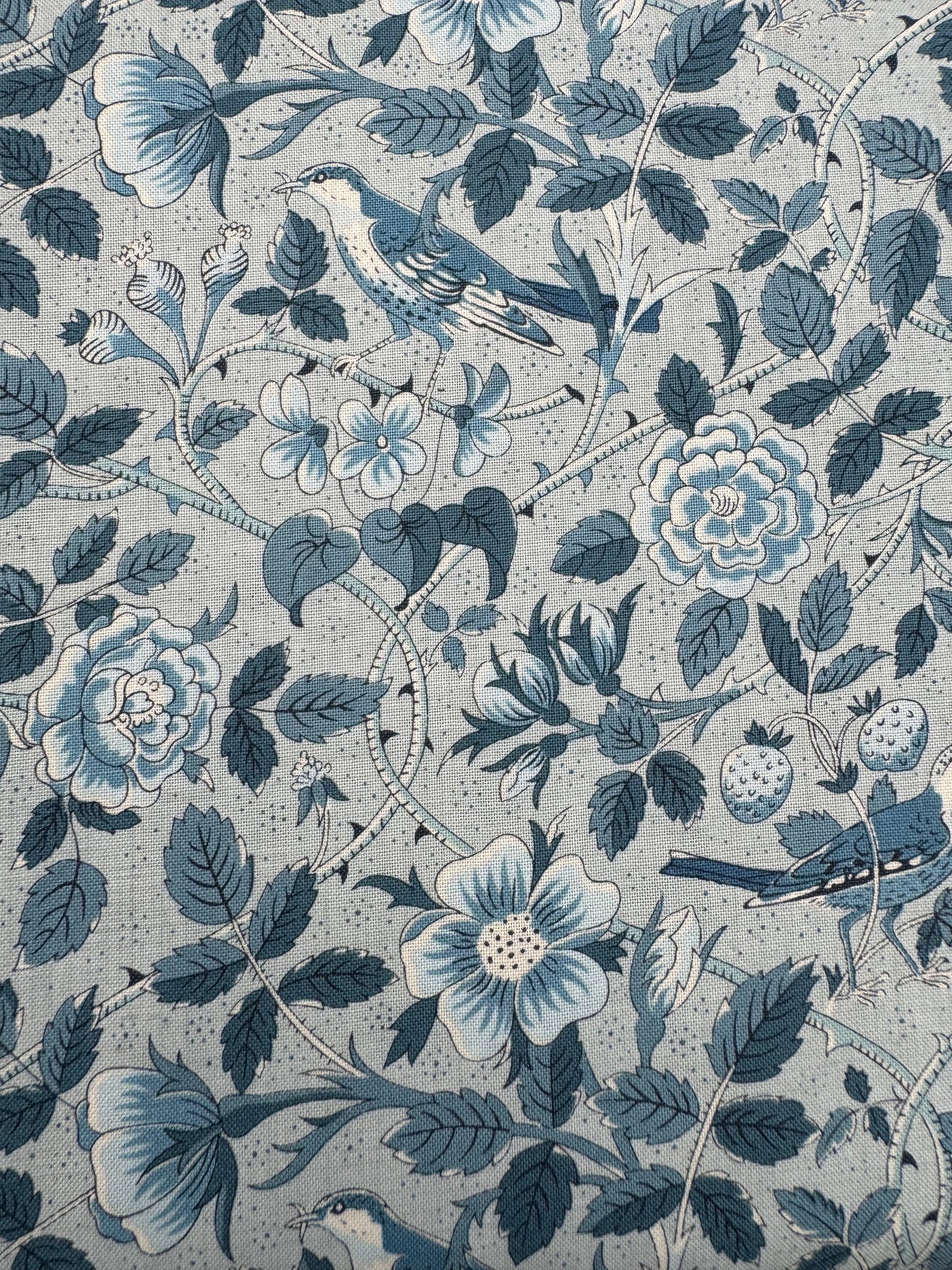 Patterned fabric with blue flowers, leaves, and birds on a light blue background