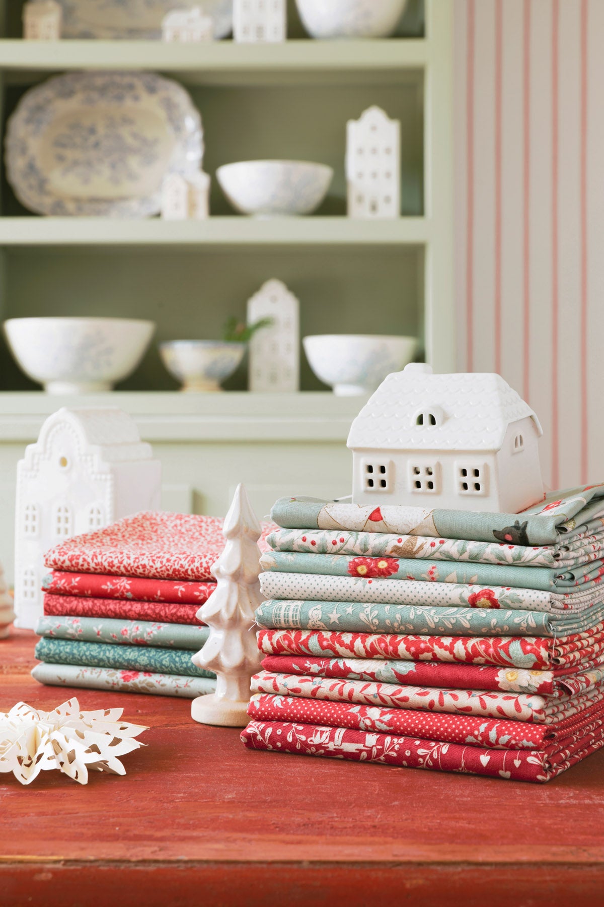 Stacks of colorful fabric rolls on a wooden surface with decorative houses and bowls in the background.