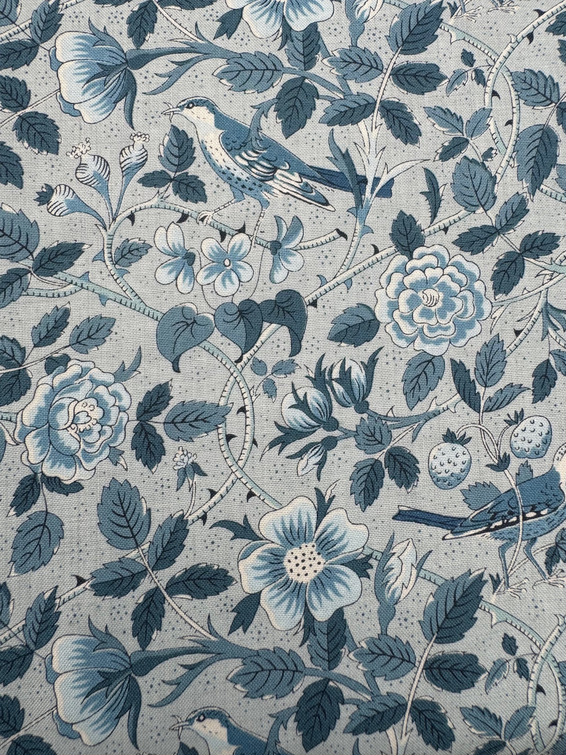 Patterned fabric with blue flowers, leaves, and birds on a light blue background