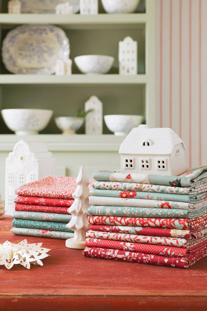 Stacks of colorful fabric rolls on a wooden surface with decorative houses and bowls in the background.